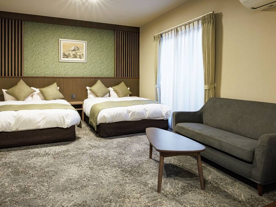 Camera d'albergo con due letti, un divano, un tavolino, una televisione a muro e un quadro incorniciato.