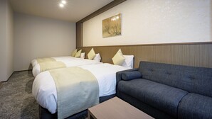 A hotel room with two beds, a sofa, a small table, and a wall-mounted artwork.