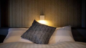 A hotel room with a patterned wallpaper, a bedside lamp, and a pillow on the bed.