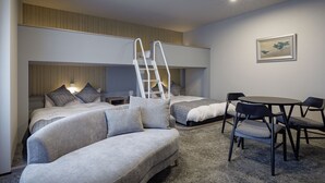 A modern hotel room with a sofa, a bed with a ladder, a small table with chairs, and a framed picture on the wall.