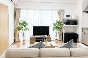 A modern living room with a flat-screen TV, a sofa, a coffee table, and two potted plants. - Casa G.S. PortVilla (Osaka-shi minato-ku chiko)