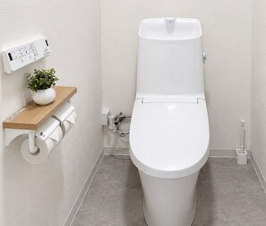 A modern bathroom with a toilet, a toilet paper holder, a small shelf with a plant, and a bidet. - Casa G.S. PortVilla (Osaka-shi minato-ku chiko)