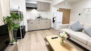 Una sala de estar moderna con un sofá, una mesa de centro, un televisor y una zona de cocina con armarios y un refrigerador.