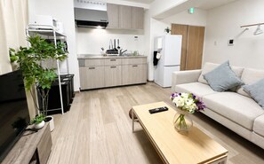 Ein modernes Wohnzimmer mit einer Couch, einem Couchtisch, einem Fernseher und einer Küchenzeile mit Schränken und einem Kühlschrank.