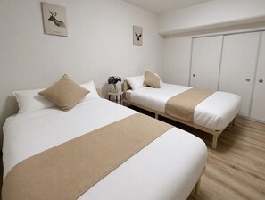 A hotel room with two beds, a small table with a vase of flowers, and a wardrobe. - Casa G.S. PortVilla (Osaka-shi minato-ku chiko)