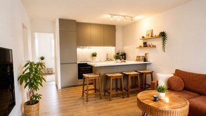 A modern living room with a sofa, coffee table, and stools. There is a kitchen area with cabinets and a countertop. - Charming apartment A stay in the heart of the Mediterranean 2 steps from the beaches (La Ciotat)