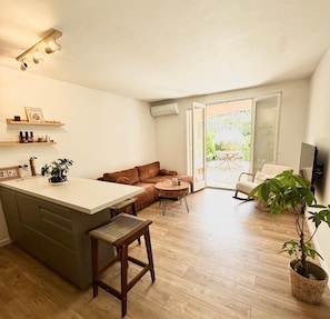 Eine moderne Küche mit einer zentralen Kochinsel, einem Essbereich mit rundem Tisch, einer Couch und einem Fernseher.