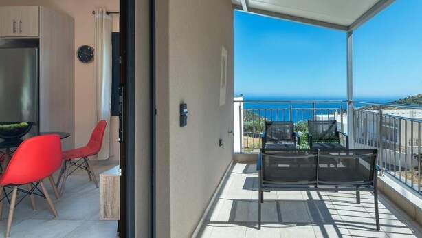 Ein Balkon mit Meerblick, ein Essbereich mit roten Stühlen und eine Küchenzeile mit Kühlschrank.