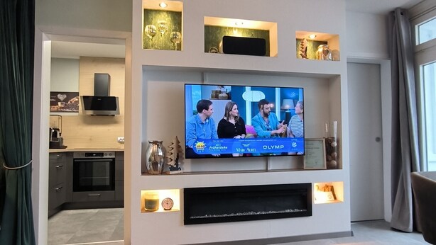 Una sala de estar moderna con un televisor de pantalla plana, un sofá, una mesa de centro y una cocina al fondo.