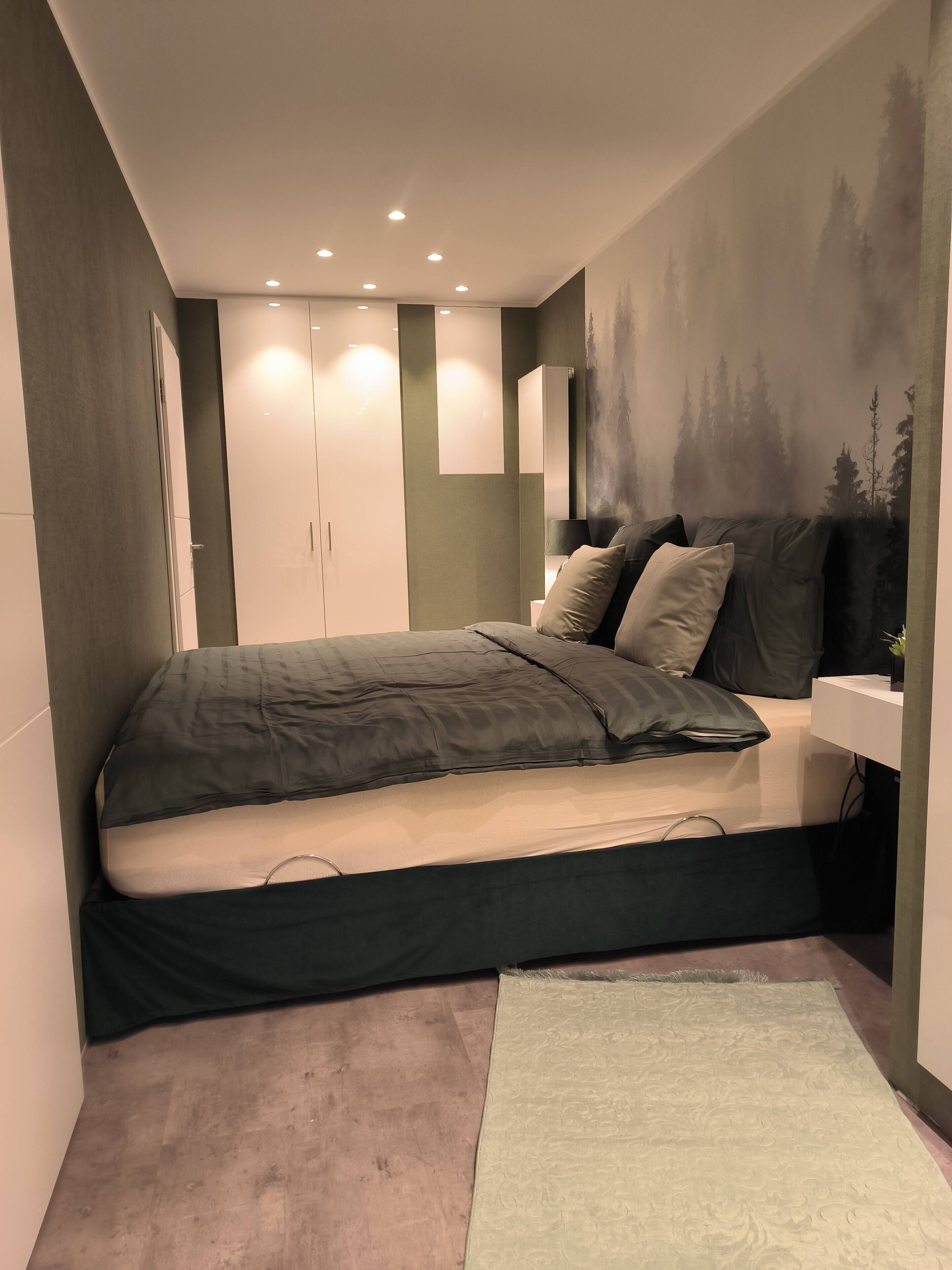 Un dormitorio moderno con cama, mesita de noche, lámpara de pared y un cuadro de árboles.