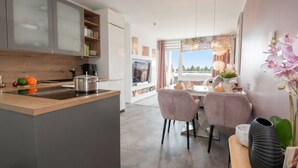 Et moderne køkken med en central ø, et spiseområde med to stole og udsigt til det fri.