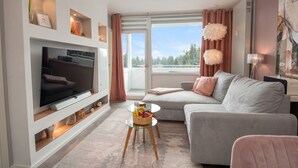 En moderne stue med et fladskærms-tv, en grå sofa og et lille rundt sofabord med frugt.