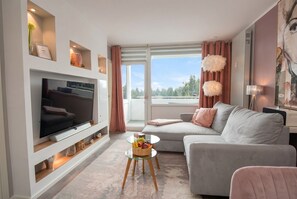 Ein modernes Wohnzimmer mit Flachbildfernseher, grauem Sofa und einem kleinen runden Couchtisch mit Obst.