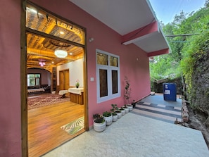 Un edifici rosa amb una porta de fusta que dona a una habitació amb sostre motllurat i un penjallum.