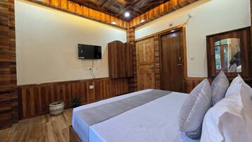 A bedroom with a wooden ceiling, a bed with pillows, a television on the wall, and a wooden wardrobe.