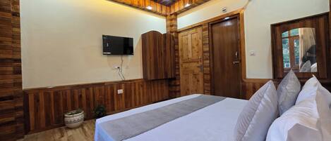 A bedroom with a wooden ceiling, a bed with pillows, a television on the wall, and a wooden wardrobe.