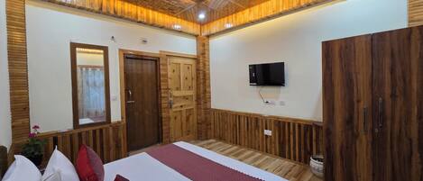 A bedroom with a wooden ceiling, a bed with white and red bedding, a TV mounted on the wall, and wooden wardrobes.