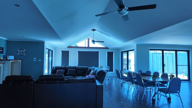 Un salon spacieux avec un plafond haut, des ventilateurs de plafond, un coin repas avec des chaises et une table, et de grandes fenêtres laissant entrer la lumière naturelle.