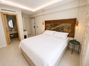 Un dormitorio con una cama grande, cabecera de madera, mesita de noche, taburete verde, espejo y un baño con tocador de madera.