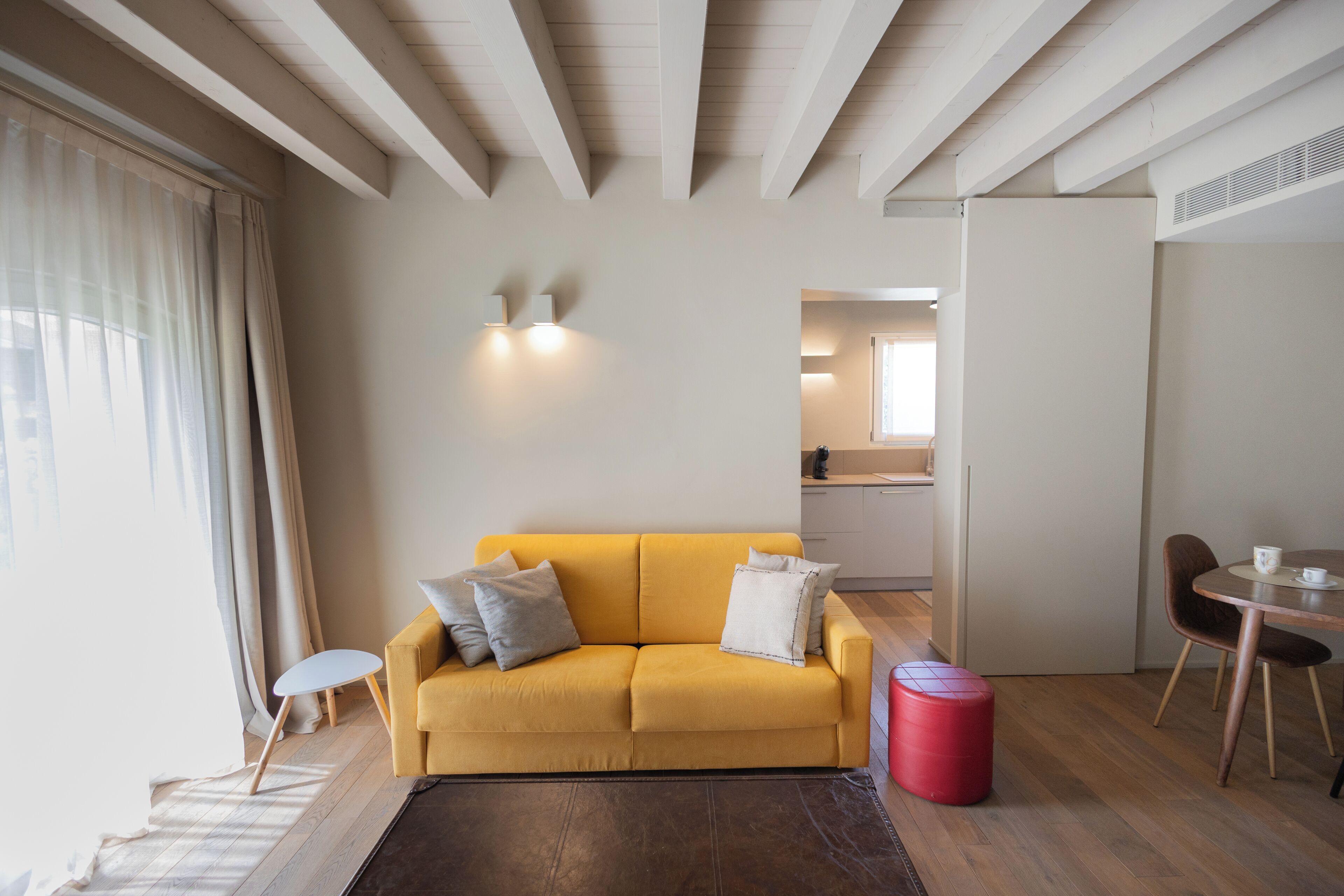 Una sala de estar moderna con un sofá amarillo, una mesita redonda y un reposapiés rojo.