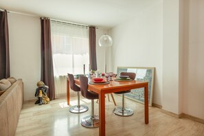 Un coin repas avec une table dressée pour deux personnes, un canapé, une statue de Bouddha décorative et une lampe sur pied.