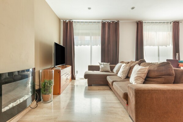A modern living room with a flat-screen TV, a sofa, a coffee table, and a fireplace.