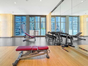 Un gimnasio con equipo de ejercicio, amplias ventanas y vistas a rascacielos.