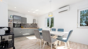 A modern kitchen with a dining area, a large window, and a ceiling light fixture. - Olive House Pool & Garden (Zemunik Donji)