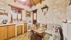 A rustic kitchen with stone walls, wooden cabinets, a dining table with chairs, and a sofa. - Villa Poseidon - Executive Suite In Zante w/Pool (Skinaria)