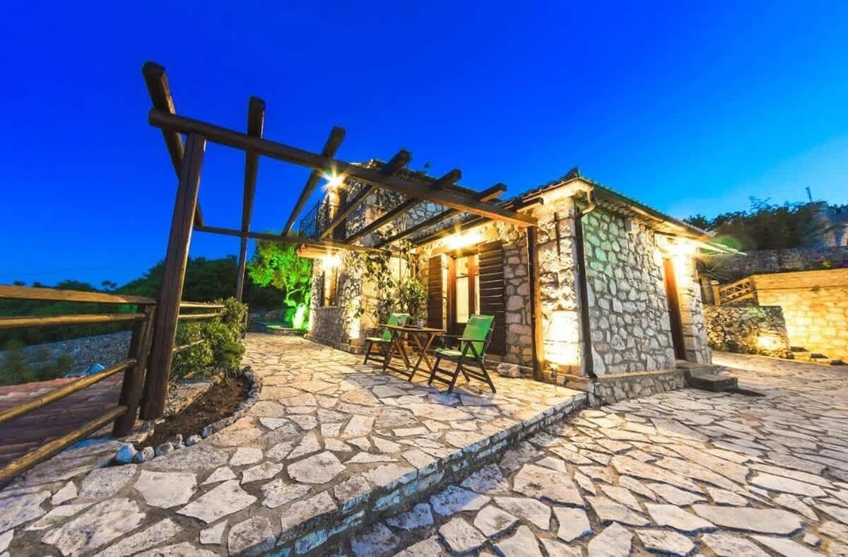 A stone building with a wooden pergola, outdoor seating, and a stone pathway.