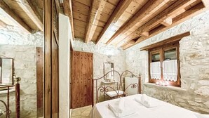 A rustic room with a bed, wooden beams, stone walls, and a window with curtains. - Villa Poseidon - Executive Suite In Zante w/Pool (Skinaria)