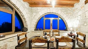A dining area with stone walls, wooden ceiling beams, and a large arched window. - Villa Poseidon - Master Suite In Zante w/Pool (Skinaria)