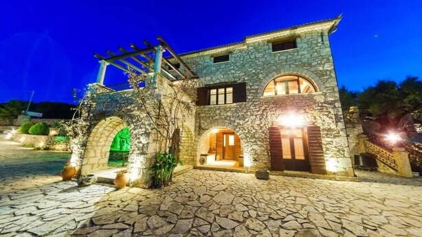 Ein Steinhaus mit Rundbogentüren und einer Pergola, beleuchtet bei Nacht.
