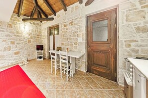 A stone-walled room with a wooden door, a white table with chairs, and a tiled floor. - Villa Poseidon - Family Suite In Zante w/Pool (Skinaria)