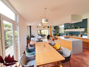Eine moderne Küche mit Kochinsel, Essbereich mit Stühlen und großen Fenstern.