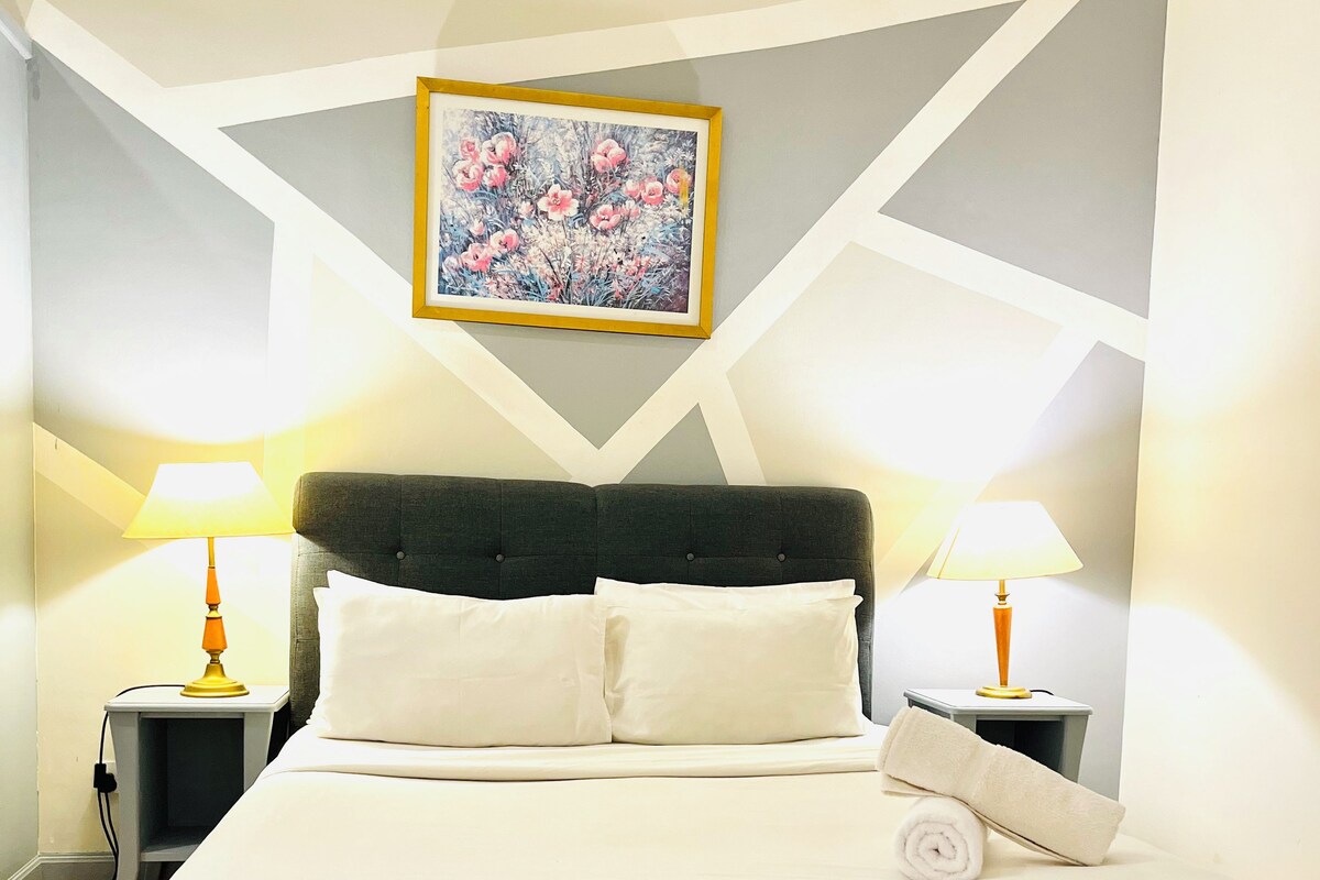 A hotel room with a bed, two bedside lamps, a painting on the wall, and a geometric wall design.