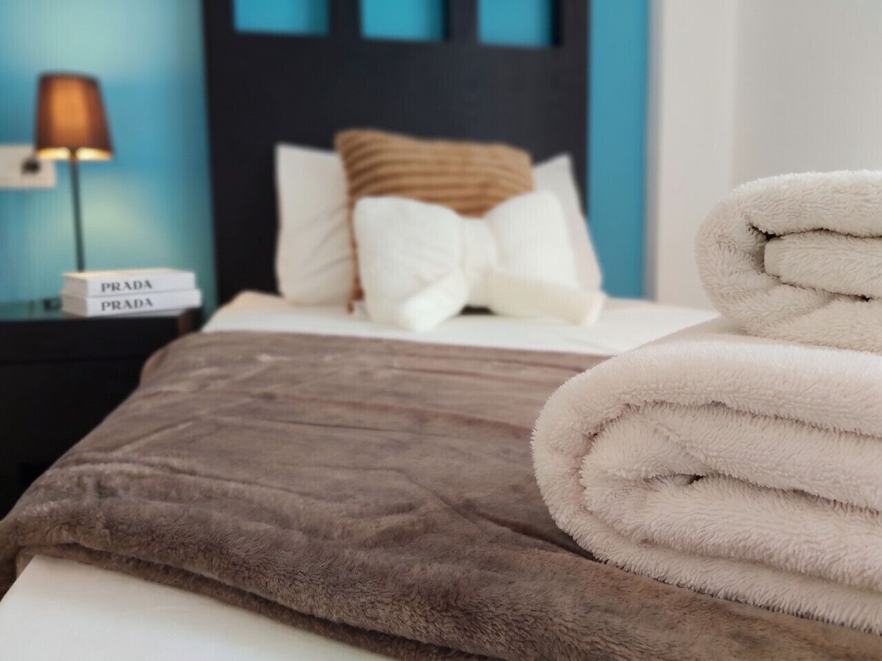 Een net opgemaakt bed met een bruine deken en een stapel witte handdoeken.