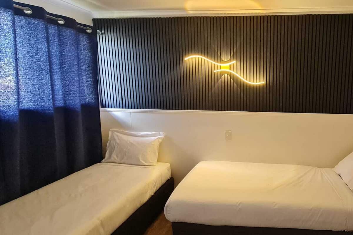 Una habitación con dos camas individuales, una pared oscura con líneas verticales y una lámpara.