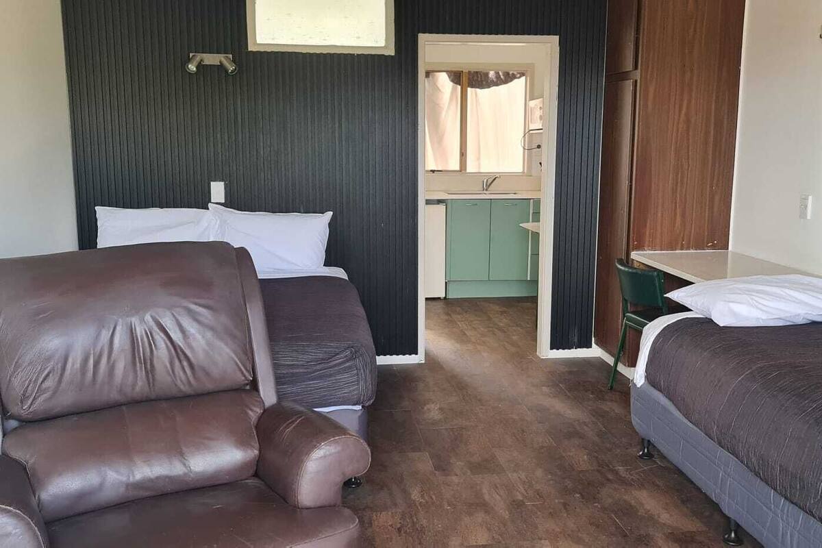Una habitación con dos camas, una silla, una mesita y un ventanal.