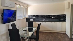 A compact kitchen with a dining area, a flat-screen TV mounted on the wall, and a window with a view.
