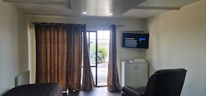 Ein Hotelzimmer mit einem Bett, einem Sessel, einem an der Wand befestigten Fernseher und einem Schrank.