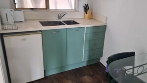 A compact kitchen with a sink, a small refrigerator, and a glass table.