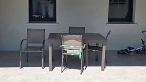 Eine Terrasse im Freien mit Tisch, vier Stühlen, zwei Fenstern und einem Fahrrad.