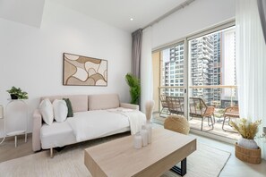A modern living room with a sofa, coffee table, and a view of high-rise buildings through large windows. - Gala Guests - Marina Views Collection (Dubai)