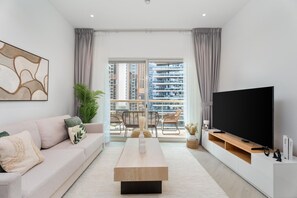 A modern living room with a sofa, coffee table, TV, and balcony with city views. - Gala Guests - Marina Views Collection (Dubai)