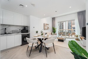 A modern apartment with a kitchen, dining area, and living room, featuring a large window with a city view. - Gala Guests - Marina Views Collection (Dubai)
