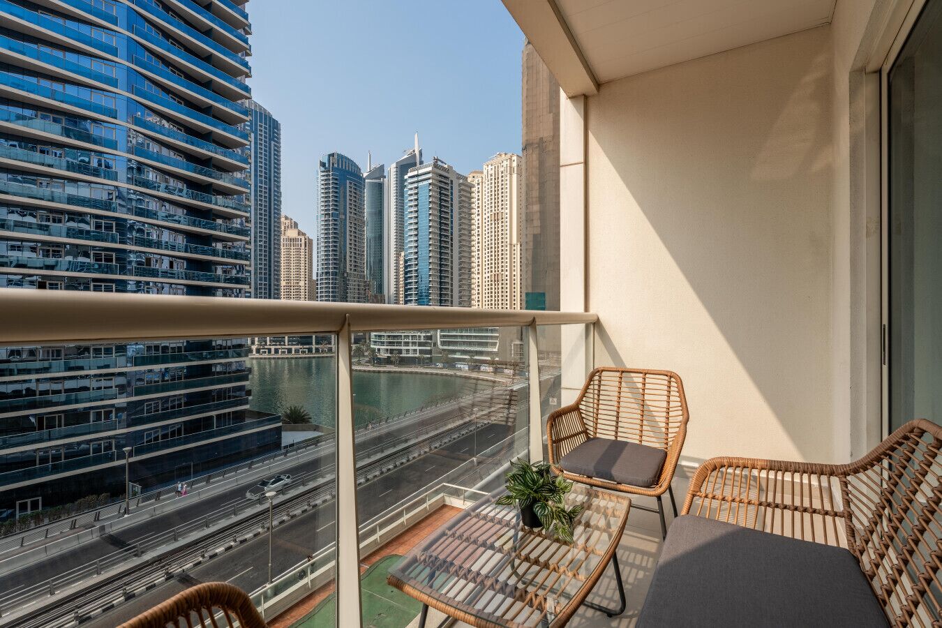 A balcony with wicker furniture, a view of a cityscape, and a body of water.