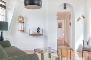 A modern living room with a green sofa, a glass coffee table, and a black pendant light. - MODERN COMFORT 2 BEDROOM APARTMENT IN HISTORIC MARAIS (Paris)