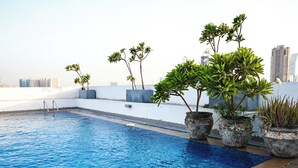 A rooftop swimming pool with potted plants and a cityscape in the background. - Bright Studio with Rooftop Pool & Gym (Dubai)