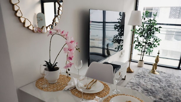 A dining table set with white plates, gold cutlery, and a potted orchid. - Bright Studio with Rooftop Pool & Gym (Dubai)